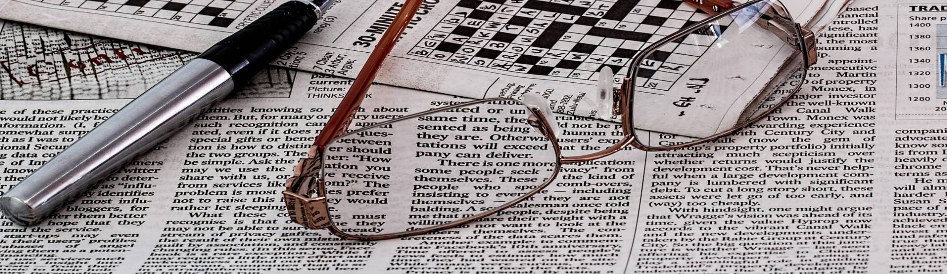 Image of newspaper, crossword puzzle, eyeglasses, and a pen